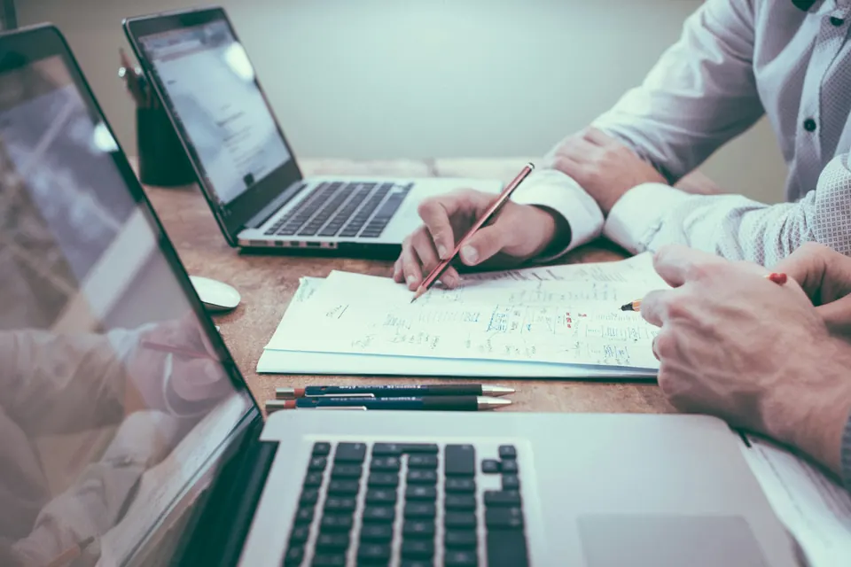 Two people planning on paper beside a laptop